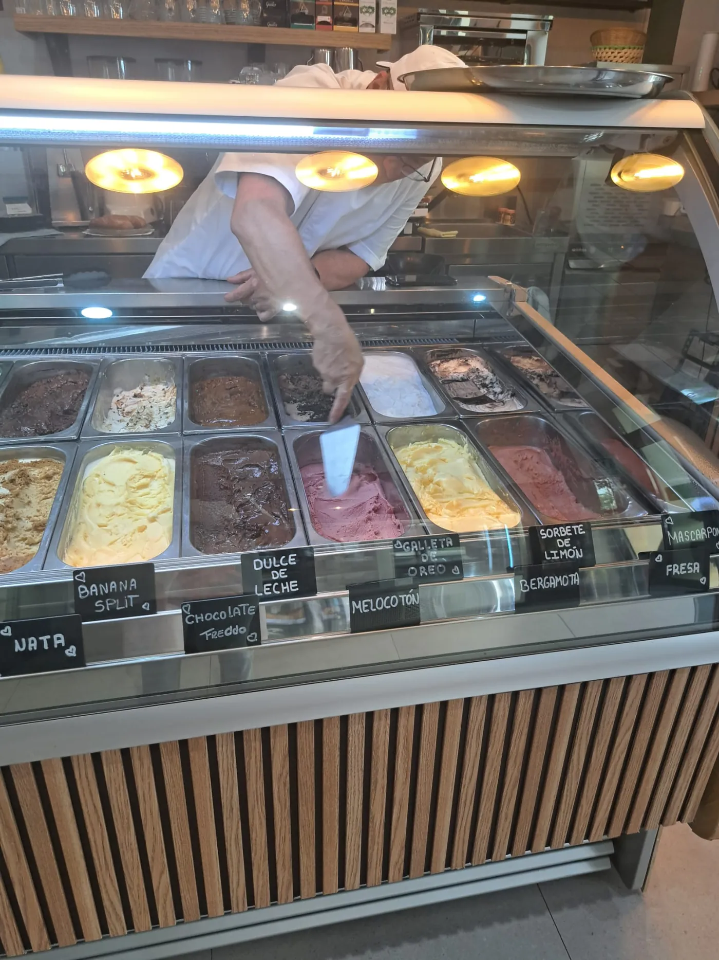 Camarera de Doca's Coffee sirviendo una bola de helado sobre la vitrina de helados